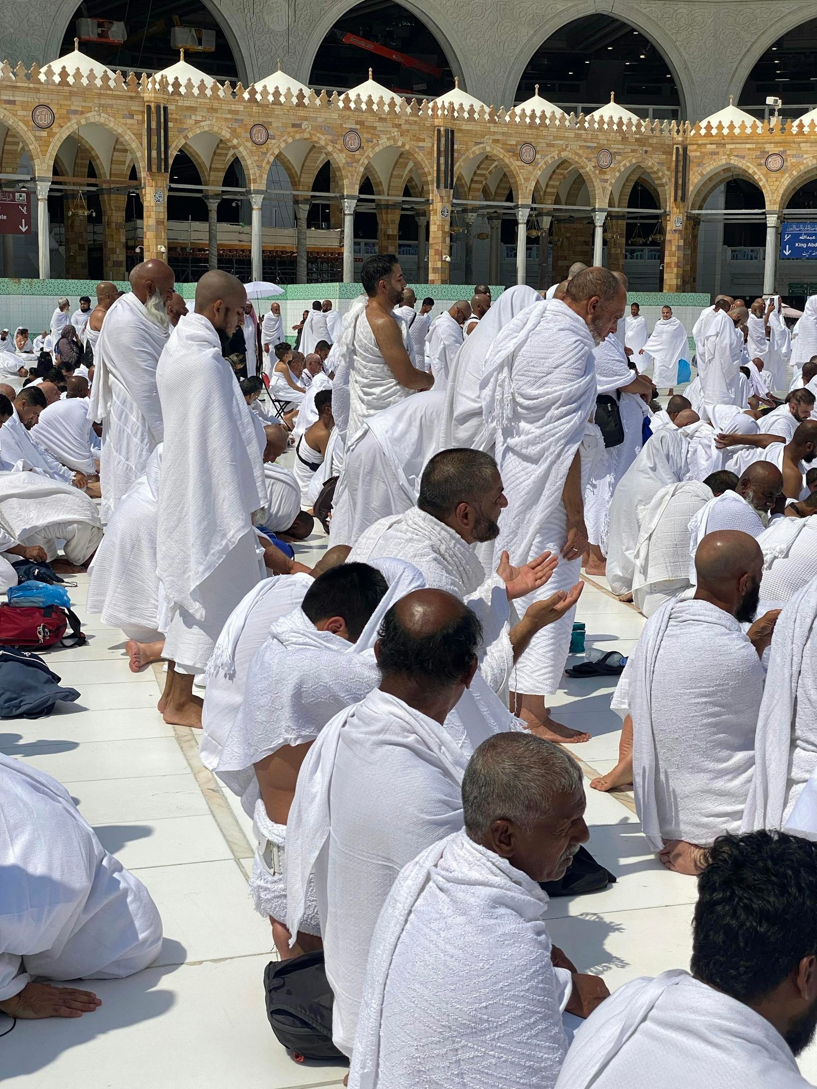 A gathering of pilgrims in white ihram garments praying at Masjid al-Haram, Mecca.