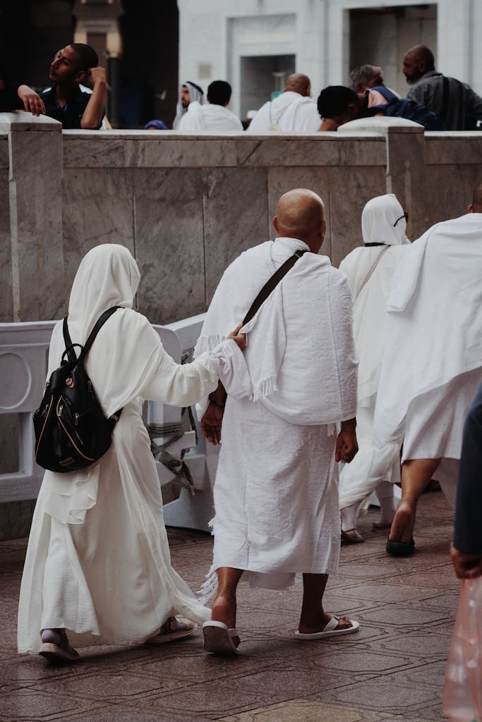 Pilgrims in traditional clothing walk together in Mecca's paved area during Hajj.
