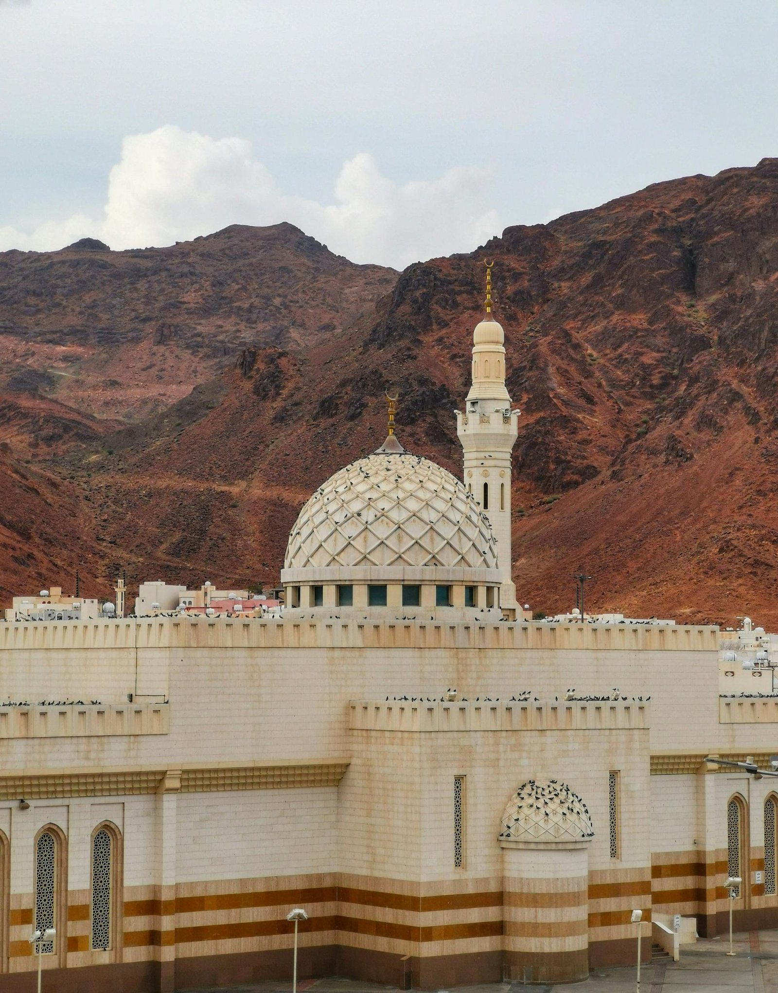 Stunning view of a mosque with minaret and mountain backdrop in Saudi Arabia.